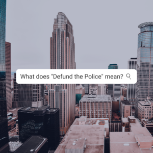 A photograph of downtown Minneapolis with the test "What does defund the police mean?"